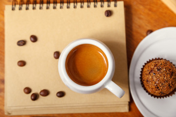A Cup of espresso with foam and a notebook, scattered coffee beans on a wooden table. Coffee break concept