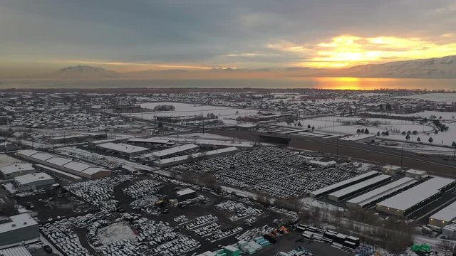 Panning aerial view over wrecking yard in winter at sunset flying over industrial area.