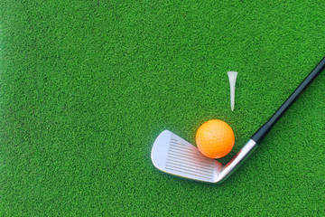 Golf equipment includes white and orange golf balls. Tee and golf clubs are placed on green grass in top view.