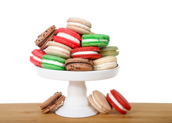 Many Christmas holiday style macaron cookies stacked on a pedestal and laying on wood table isolated on white. Minimalist design.