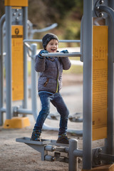 Six years old boy work out at the outdoor gym. The device has instructions for use in Polish.