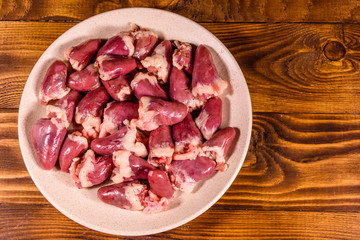 Ceramic plate with raw chicken hearts on wooden table. Top view