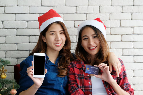 Two young cute asia women holding smart phone with blank screen and credit card for shopping online background,mock up, with happiness, Christmas holiday shopping concept