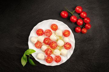 Fototapeta na wymiar An overhead photo of a plate of Caprese salad with Mozzarella cheese, cherry tomatoes, and fresh basil leaves, shot from above on a black background with a place for text
