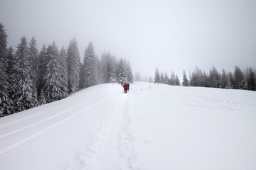 Footpath in snow and hikers going up on snowy slope