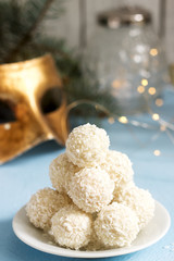 Coconut candies with white chocolate on a winter background with a garland, a candle and fir branches.