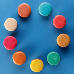 Colorful french macaroons on a blue background laid out in a circle. Dessert with tea or coffee.