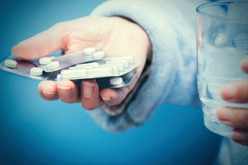 elderly hand of a senior is holding pills, water glass and blister pack