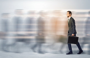 Young businessman with briefcase hurry up on a crowded street with blurred people around
