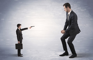 Fototapeta premium Tiny businessman with gun shooting giant fearful businessman 