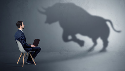 Humble businessman staying and offering stuffs to a huge angry bull shadow
