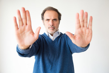 Serious handsome middle aged man making stop gesture. Mature man gesturing forbidden with two hands. Isolated on white. Prohibition concept