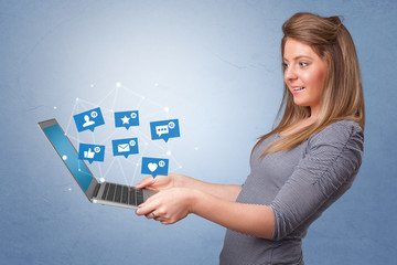 Woman holding laptop with different types of social media symbols and icons
