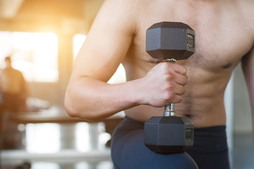Closeup image of man lifting dumbbells in front of dirty wall background at old gym. - Image