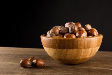 Obraz premium Hazelnuts in wooded bowl isolated on black background, copy space