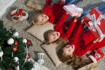 three girls lie near a Christmas tree with gifts new year holiday winter