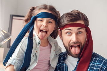 Father and little daughter at home sitting wearing ties tongue out grimace