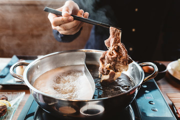Man holding medium rare slice Wagyu A5 beef out from hot pot shabu shoyu soup base by chopsticks...