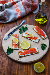 Sandwich with salmon, lemon and herbs on a wooden round board