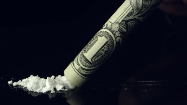 Line of cocaine being snorted up rolled up dollar bill on black reflective table top.