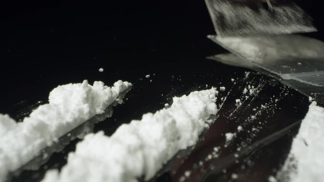 Moving over rows of cocaine as lines are cut with razor blade viewing the white powder drug.