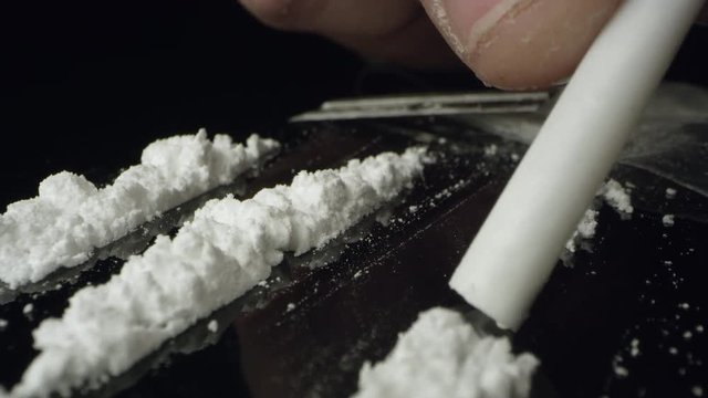 Lines of cocaine being snorted through tube on table top while moving over the white powered drug.