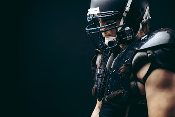 Fototapeta na wymiar Shirtless American football player with wearing helmet and protective shields on naked body, half size portrait over black wall, close up