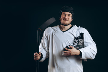 Smiling hockey player looking at camera with skates over shoulder. Isolated on blue