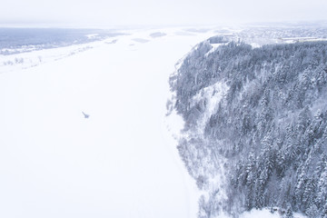Aerial view of the forest and river at winter. Flying drone over the frozen snowy river.