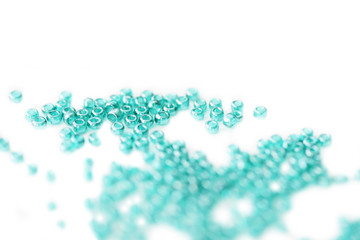 Seed beads of aquamarine color scattered on white surface close up
