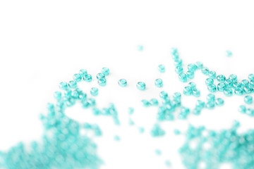 Seed beads of aquamarine color scattered on white surface close up