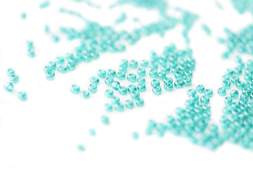 Seed beads of aquamarine color scattered on white surface close up