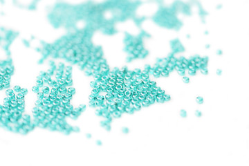 Seed beads of aquamarine color scattered on white surface close up