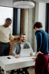Obraz premium Group of three young multiethnic entrepreneurs standing in the office while debating and discussing new start-up project