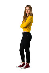 A full-length shot of a young girl with yellow sweater keeping the arms crossed in lateral position while smiling on isolated white background