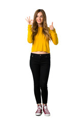 A full-length shot of a young girl with yellow sweater showing ok sign with and giving a thumb up gesture on isolated white background