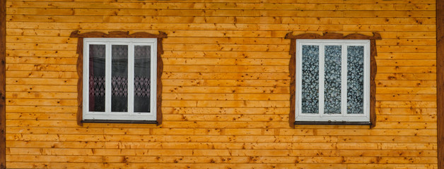 Two white wooden windows in the wall of raw brown wooden boards with knots. Frontal view. Close-up.
