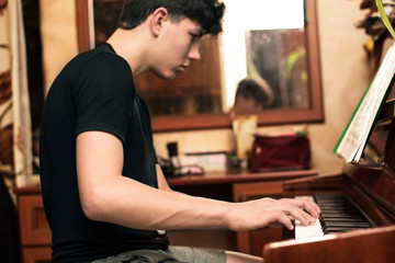A teenage boy with dark hair plays a piano at home. Focus on hands
