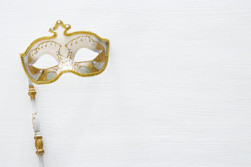 carnival party celebration concept with elegant gold mask on stick over white wooden background. Top view.