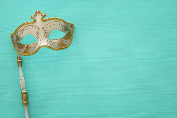 carnival party celebration concept with elegant gold mask on stick over mint wooden background. Top...