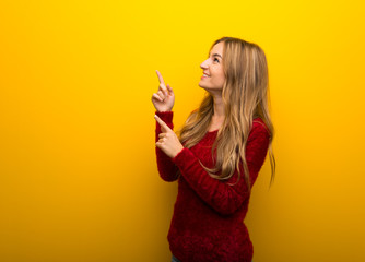 Young girl on vibrant yellow background pointing with the index finger and looking up