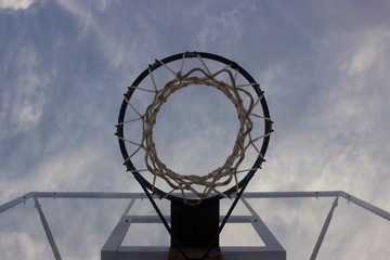 Look at the blue cloudy sky trough a basketball ring with net and transparent glass board 