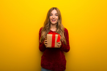 Young girl on vibrant yellow background surprised because has been given a gift