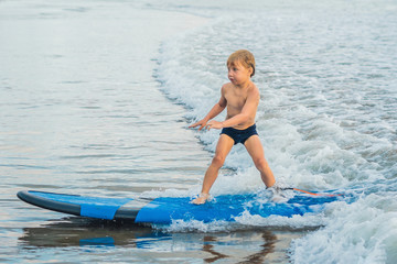 Little boy surfing on tropical beach. Child on surf board on ocean wave. Active water sports for...