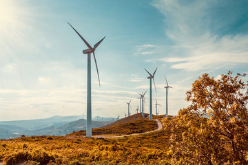 Wind turbines on beautiful sunny summer autumn mountain landsape. Curvy road through mountain Eolic park. Green ecological power energy generation. Wind farm eco field