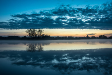 Fog on the lake, trees on the shore and clouds