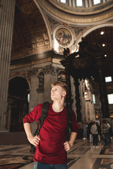 Fototapeta na wymiar Portrait of a young tourist man in the Basilica Sancti Petri. Tourist stands in the church and looks at the sides.