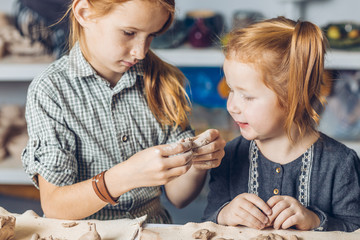 two ginger adorable girl making a shape to a product in the art lesson. close up photo. free time activity