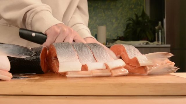 Close-up of female hands are cutting with a knife a large salmon on a wooden table of home cooking