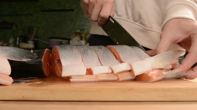 Close-up of female hands are cutting with a knife a large salmon on a wooden table of home cooking